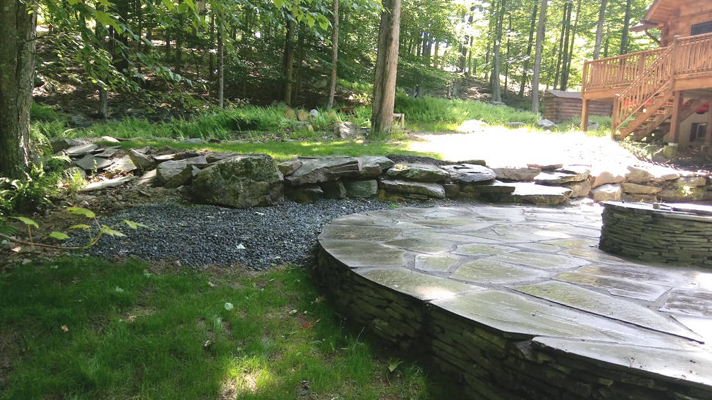 Repaired Round Bluestone Patio with Firepit and Boulder Retaining Wall by Apple Creek Landscaping, LLC.